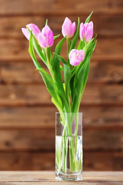 Lindas tulipas cor-de-rosa em vaso na mesa sobre fundo de madeira — Fotografia de Stock