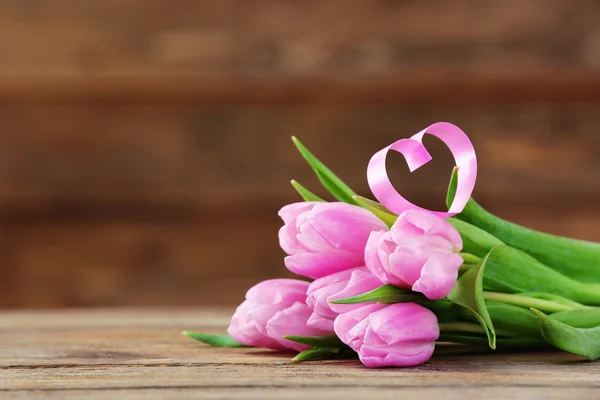 Mooie roze tulpen met decoratieve hart op houten achtergrond — Stockfoto