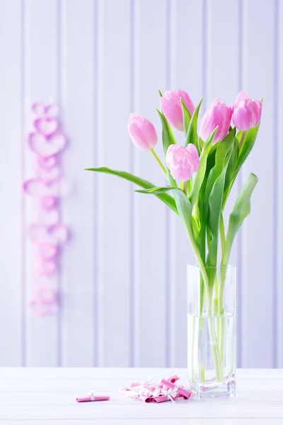 Belas tulipas cor-de-rosa em vaso com corações decorativos em fundo de madeira — Fotografia de Stock