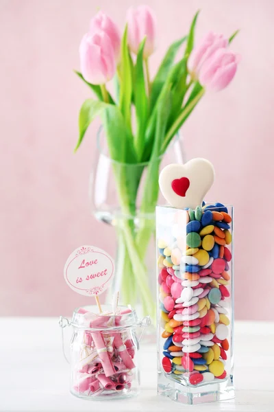 Krásné růžové tulipány s sladkosti ve váze na stole na světlé pozadí — Stock fotografie