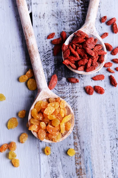 Pasas y Goji en cucharas sobre fondo de mesa de madera de color — Foto de Stock