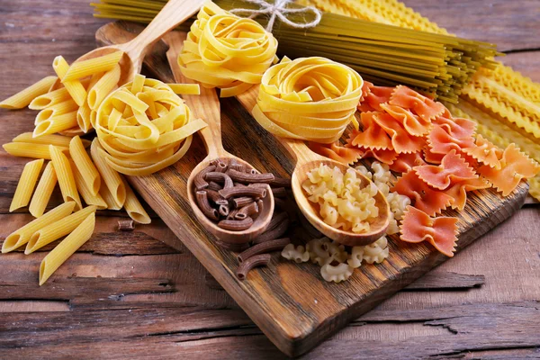 Diferentes tipos de pasta sobre tabla de cortar y fondo de mesa de madera —  Fotos de Stock