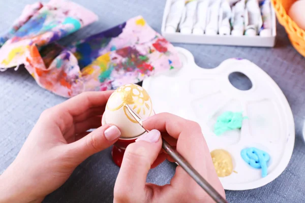 Painting Easter eggs by female hands on colorful tablecloth background — Stock Photo, Image