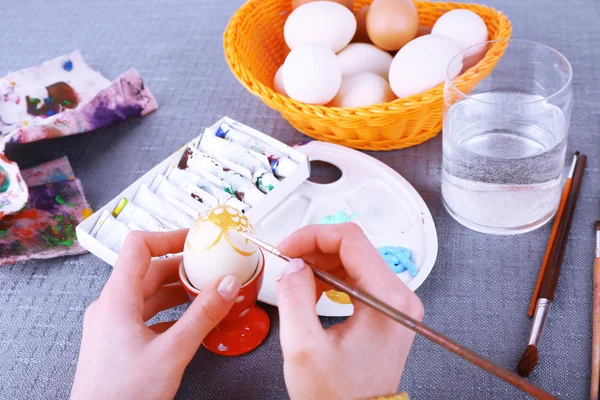 Живопись пасхальных яиц женскими руками на цветном фоне скатерти — стоковое фото