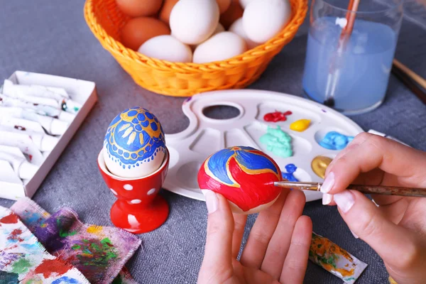Pintura de huevos de Pascua por manos femeninas sobre fondo de mantel colorido —  Fotos de Stock