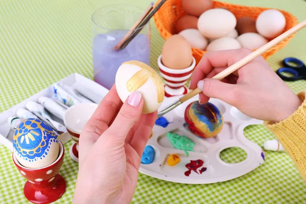 Pintura de ovos de Páscoa por mãos femininas em fundo de toalha de mesa colorido — Fotografia de Stock