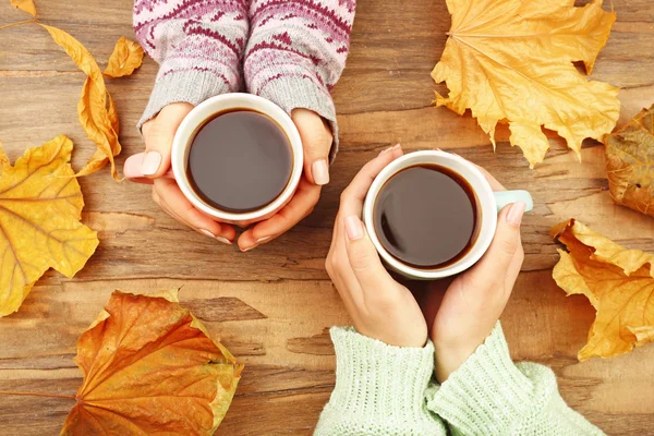 Mano femminile che tiene tazze di caffè con foglie autunnali su sfondo tavolo in legno rustico — Foto Stock