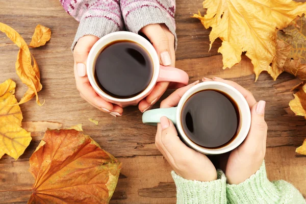 Mão feminina segurando xícaras de café com folhas de outono no fundo da mesa de madeira rústica — Fotografia de Stock