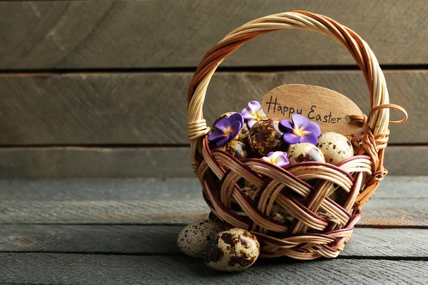 Ovos de pássaro em cesta de vime com flores decorativas em fundo de madeira — Fotografia de Stock