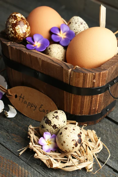 Bird eggs in wooden bucket with decorative flowers on wooden background — Stock Photo, Image