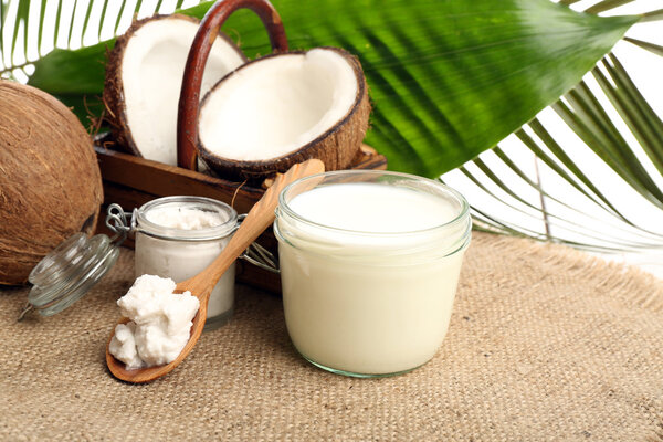 Coconut with jars of coconut oil and  milk on sackcloth on natural background