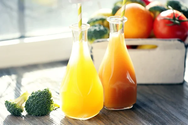 Bottles of juice with fruits and vegetables  in crate on windowsill — Stock Photo, Image