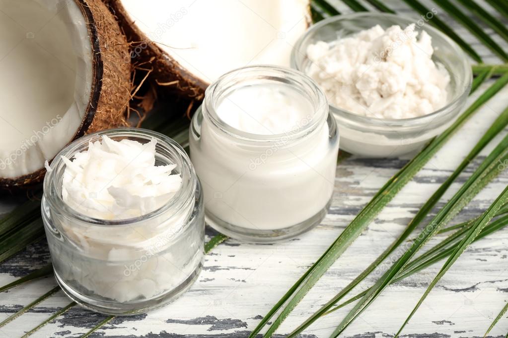 Coconut with jars of coconut oil and cosmetic cream on wooden background