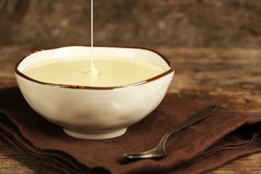 Bowl with condensed milk on napkin on wooden background clipart