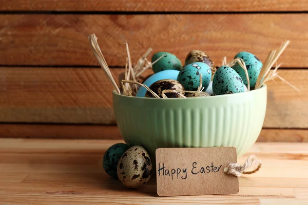 Bird colorful eggs in bowl on wooden background — Stock Photo, Image