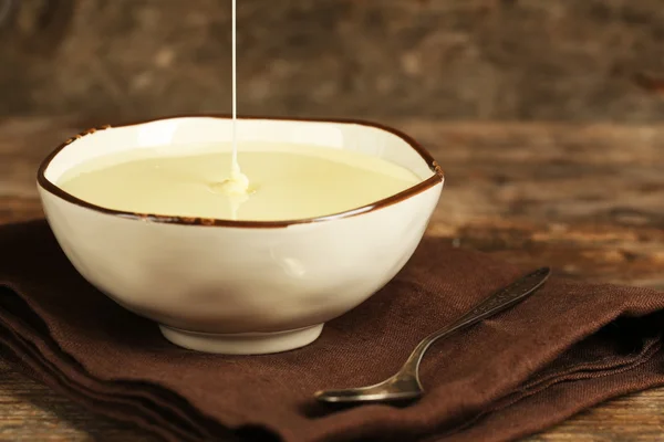 Bowl cu lapte condensat pe șervețel pe fundal din lemn — Fotografie, imagine de stoc