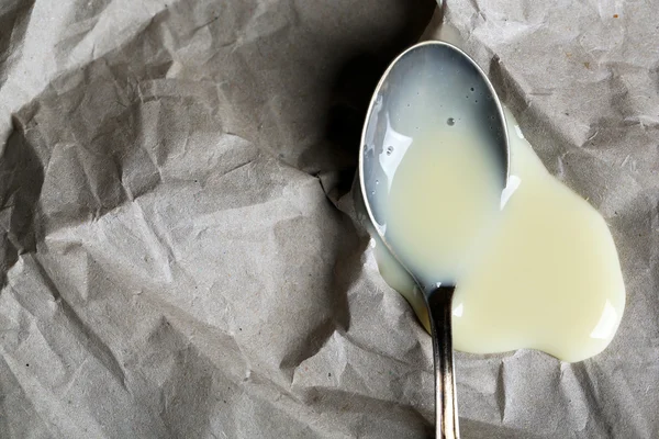 Spoon with condensed milk on paper background — Stock Photo, Image