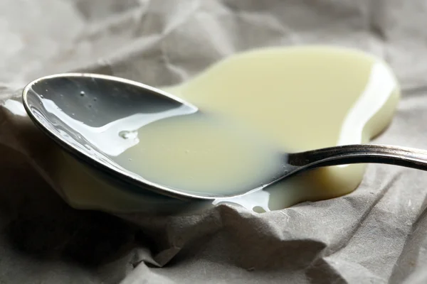 Spoon with condensed milk on paper background — Stock Photo, Image