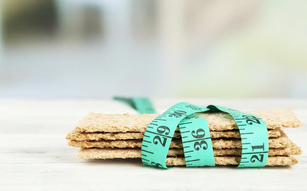 Fresh crispbread with measuring tape, on wooden table- diet concept — Stock Photo, Image