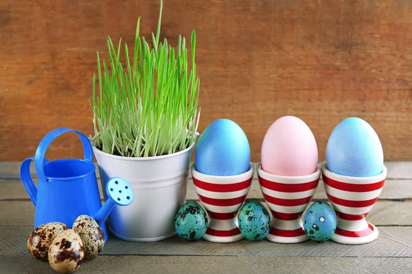 Césped verde fresco en cubo de metal pequeño y huevos de Pascua en los titulares, sobre fondo de madera — Foto de Stock