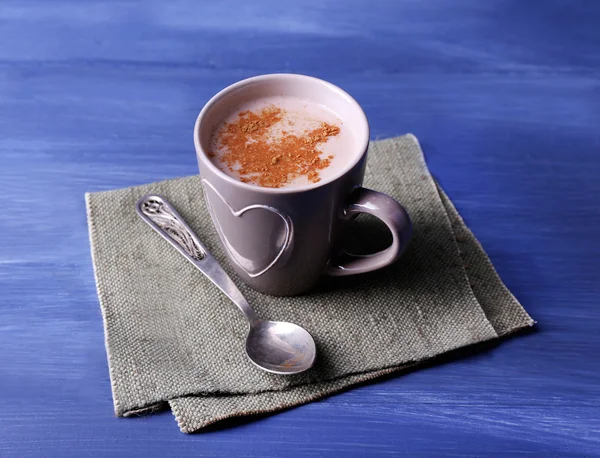 Cup of cocoa with spoon on burlap cloth on color wooden background — Stock Photo, Image