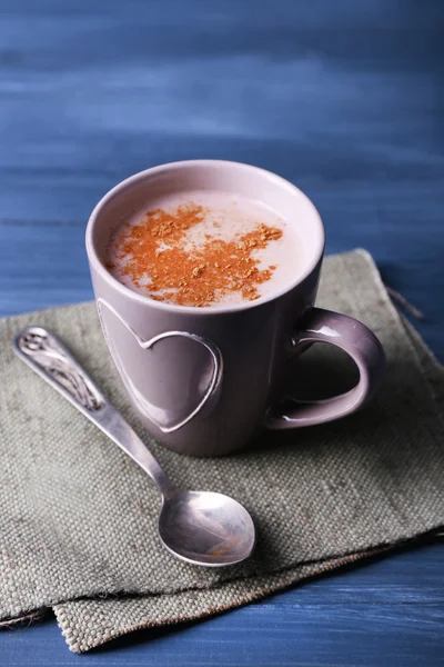 Cup of cocoa with spoon on burlap cloth on color wooden background — Stock Photo, Image
