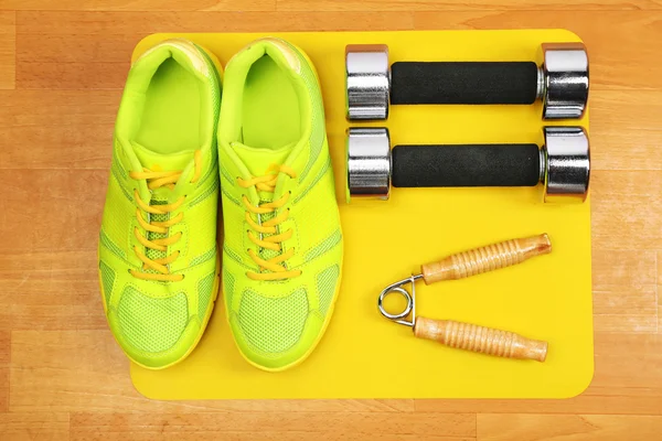 Shoes and sports equipment on mat on wooden floor, top view — Stock Photo, Image