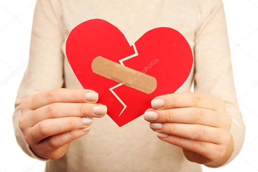 Woman holding broken heart with plaster close up