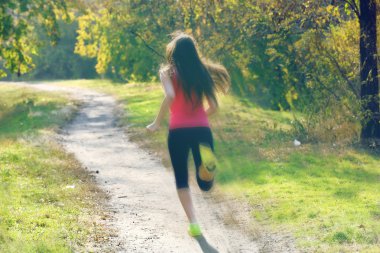 Genç bir kadın parkta koşuyor.