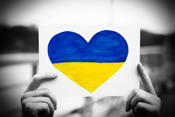 Hands holding paper heart with painted Ukraine flag