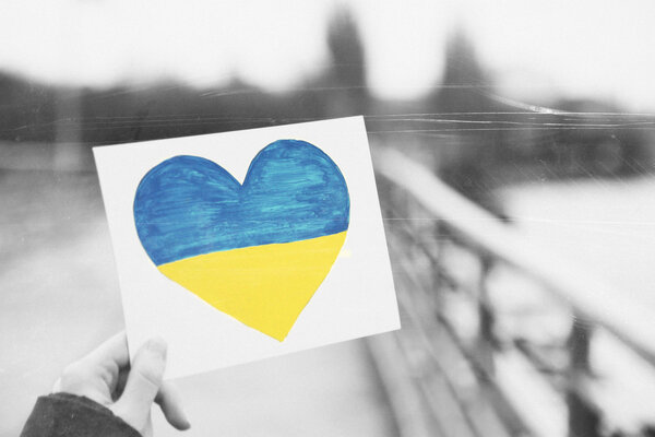 Hands holding paper heart with painted Ukraine flag