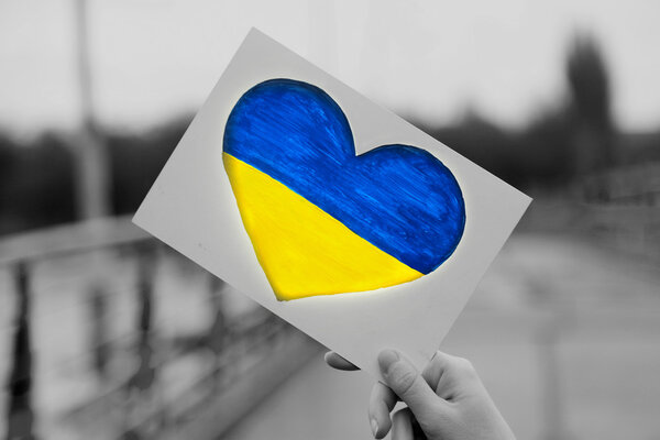 Hands holding paper heart with painted Ukraine flag