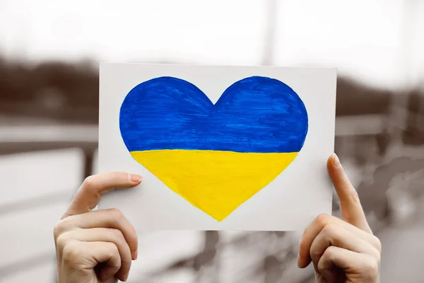 Руки держат бумажное сердце с окрашенным флагом Украины — стоковое фото