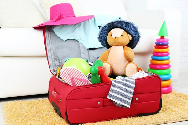 Suitcase packed with clothes and child toys on fur rug and white sofa background — Stock Photo, Image