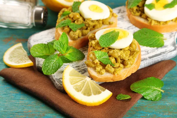 Sandwiches with green peas paste and boiled egg on cutting board with napkin on color wooden background — Stock Photo, Image