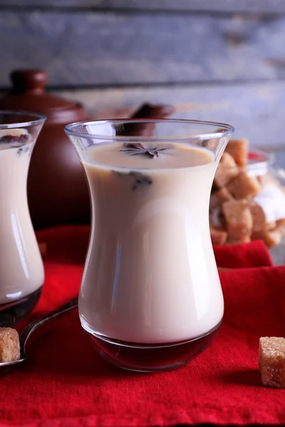 Té negro con leche en vasos y tetera con azúcar en terrón sobre fondo de tablones de madera de color —  Fotos de Stock