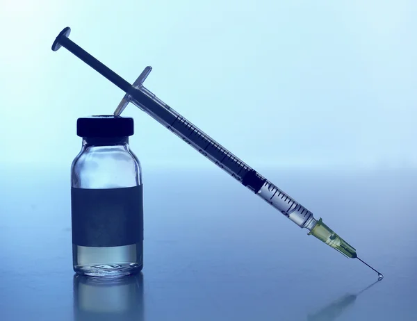 Ampoule médicale avec seringue sur fond bleu — Photo