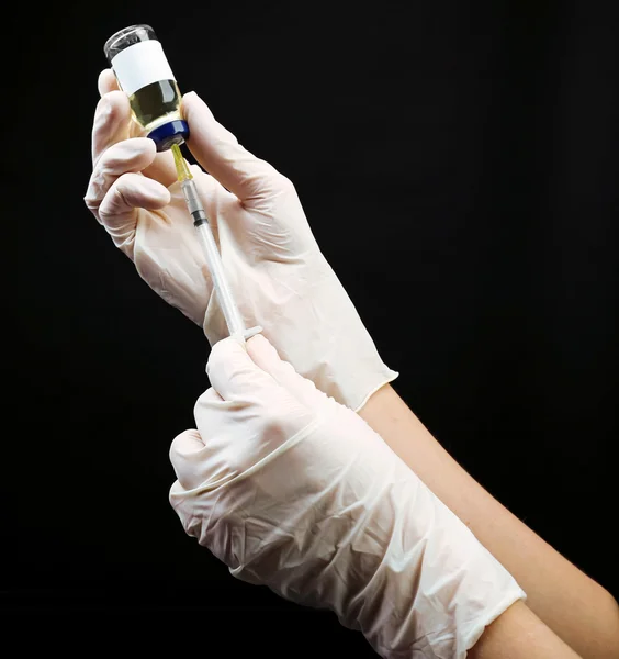 Manos en guantes llenando medicamentos de ampolla en jeringa sobre fondo negro — Foto de Stock