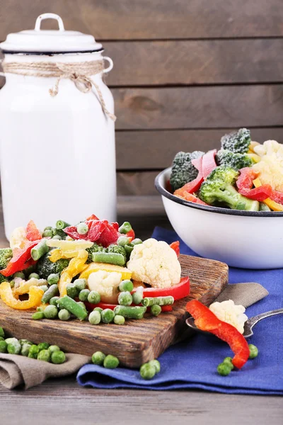 Verduras congeladas sobre tabla de cortar, sobre servilleta, sobre fondo de mesa de madera —  Fotos de Stock