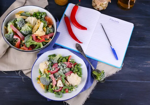 Frozen vegetables and blank notebook, on wooden table background — Stock Photo, Image