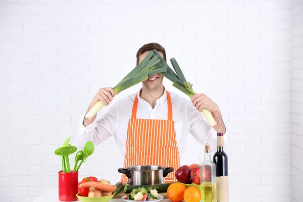 Uomo a tavola con diversi prodotti e utensili in cucina su sfondo bianco a parete — Foto Stock