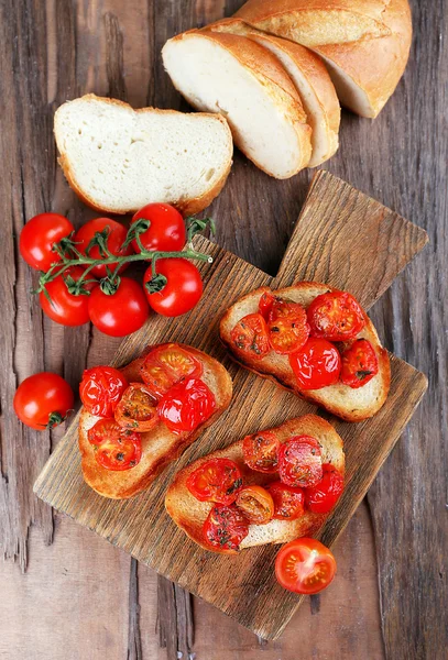 Fatias de pão tostado branco com tomates enlatados na tábua de corte no fundo da mesa de madeira — Fotografia de Stock