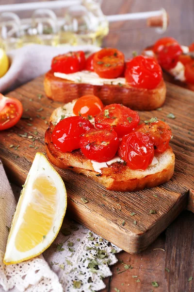 Fette di pane bianco tostato con pomodori in scatola e lime sul tagliere su sfondo tavolo di legno — Foto Stock