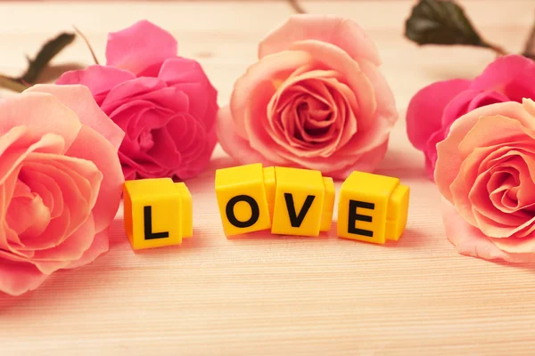 Beautiful roses with word LOVE on wooden background — Stock Photo, Image