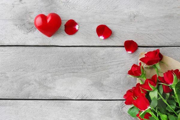 Красные розы, завернутые в бумагу с сердцами на деревянном фоне стола — стоковое фото