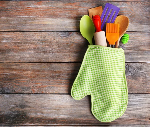 Set of kitchen utensils in mitten on wooden planks background — Stock Photo, Image