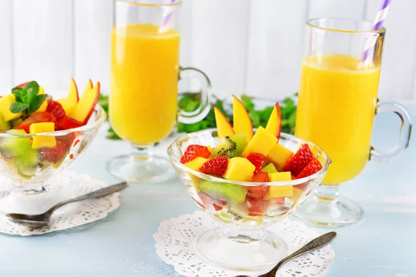 Фруктовый салат с мятой и апельсиновым соком в стеклянной посуде на деревянном столе и фоне досок — стоковое фото