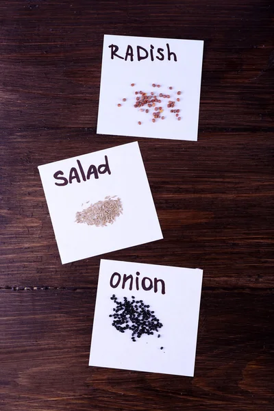 Different seeds on pieces of paper on wooden background