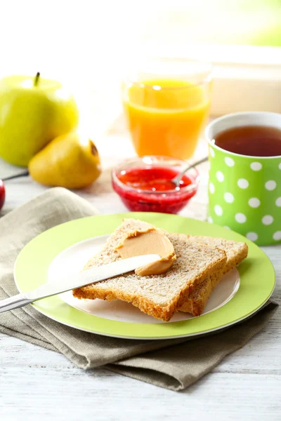 Toasts with peanut butter on plate with cup of tea and juice on light background — Stock Photo, Image