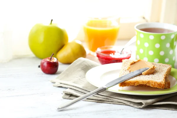 Pirítós peanut butter, a tányér csésze tea és gyümölcslé-ra könnyű háttér — Stock Fotó
